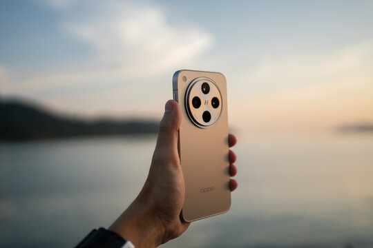 PENANG, MALAYSIA - JAN 02, 2025: Close-up of a hand holding an OPPO Find X8 smartphone showing large circular Hasselblad camera module against a soft sky and water background.