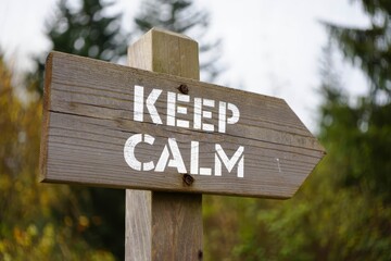 Vintage and rustic wooden signpost with the weathered text quote keep calm, outdoors in nature. blurred out forest fall colors in the background.