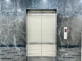 Modern elevator with closed stainless steel doors in a luxury building. Elegant marble wall with glossy finish reflecting minimalist and contemporary architectural interior design. © Jreacher