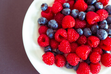 Top view of fresh blueberries and raspberries on a white plate with soft light. Simple and vibrant fruit composition for summer themes.