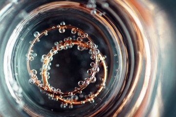 Macro view through a glass of two intertwined wedding rings with air bubbles, creating a surreal, abstract visual with reflections and circular patterns.