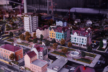 A detailed miniature model of a cityscape featuring colorful buildings, trees, and roads. The scene includes a roundabout and various architectural styles, showcasing urban planning.