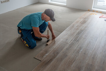Floating floor work. The worker's hands taps the board of vinyl plank to lock the click system. He is using hammer and wooden plank.