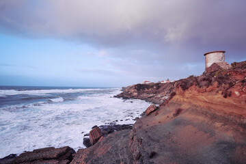 A scenic coastal landscape with rocky cliffs, a lighthouse in the distance, and a cloudy sky.