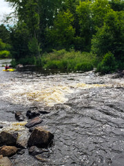 a whitewater rapids river scene with a blurred kayaker in the distance. nature and recreation design element with copy space