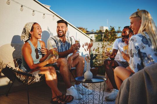 Cheerful friends laughing and enjoying refreshing drinks on a sunny rooftop terrace