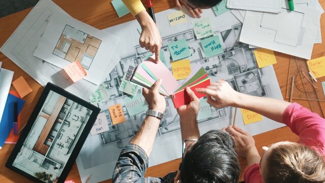 Top down aerial view of interior designer team choosing color from palettes while architect engineer planning house construction from tablet and project plan at table with building plan. Symposium. - Powered by Adobe