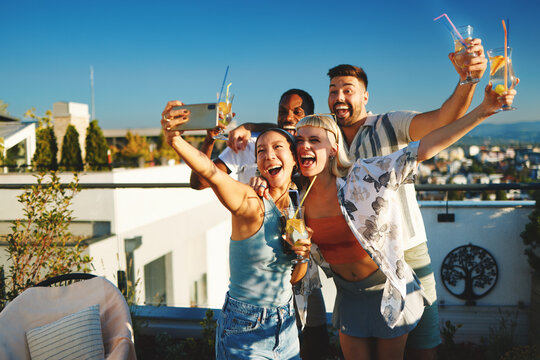 Group of cheerful multi-ethnic friends taking selfie at rooftop party, enjoying summer sunset - Powered by Adobe