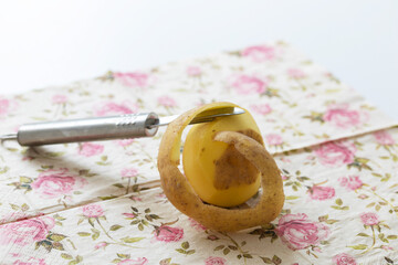 A potato lying on a cloth napkin and a knife cutting the potato skin.