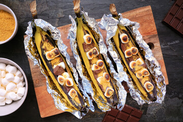 Summer campfire banana smores. Overhead view table scene over a dark background. © Jenifoto