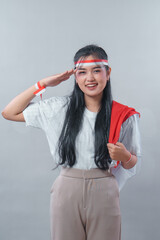 Smiling Indonesian woman giving a patriotic salute while wearing a red and white headband and...