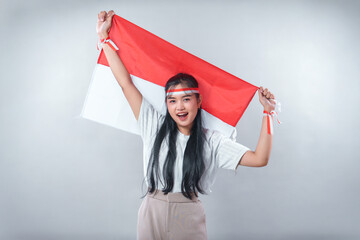 Happy Indonesian woman raising the red and white flag proudly, smiling with energy and enthusiasm,...