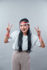 Energetic young Indonesian woman showing double peace signs with a cheerful smile, wearing red and...