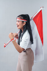 Excited young Asian woman showing enthusiastic gesture while holding Indonesian flag, celebrating...