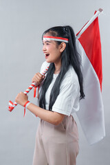 Energetic young Asian woman smiling with Indonesian flag, wearing red and white accessories to...
