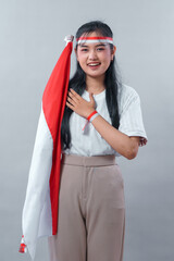 A smiling Asian woman wearing a red and white headband proudly poses with the Indonesian flag,...