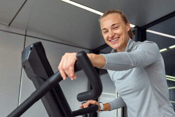 Smiling woman exercising on elliptical trainer indoors at modern fitness center