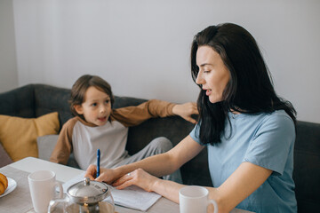 Mother helping son with homework at home during breakfast