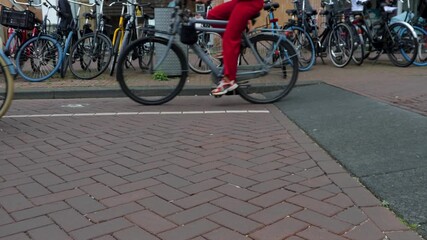 Bikes passing by in downtown Amsterdam, you can only see the wheels and feet on a cloudy day in summer