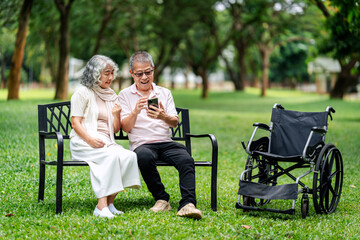 Elderly senior couple happily using smartphone outdoors on park bench enjoying leisure time technology connection retirement wellbeing