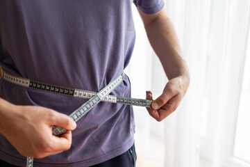 man  measures waist size. concept of fighting excess weight and obesity, social standards of...