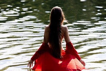 Elegant woman in red dress, back view by the lake