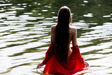Elegant woman in red dress, back view by the lake