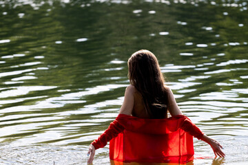 Elegant woman in red dress, back view by the lake