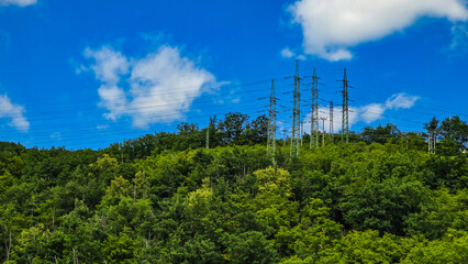 High voltage power lines against the background of green forest and bright blue sky with clouds....
