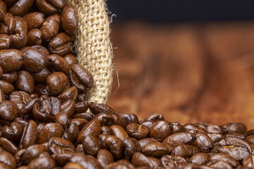 Roasted coffee beans spill from a jute bag onto a rustic wooden surface.