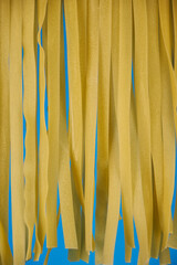 Fresh egg fettuccine noodles, drying in the foreground against a light blue background with copy space