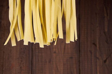 Fresh egg fettuccine noodles, drying in the foreground with a handmade wooden background with copy...