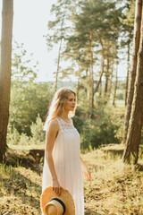 Blonde woman holding a straw hat enjoying nature in a pine forest