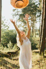 Happy woman throwing straw hat in the air in a forest