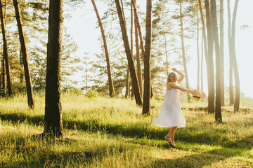 Happy woman dancing and holding her straw hat in a sunny pine forest