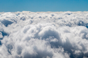 Naklejka premium Aerial view of Large, fluffy cumulus clouds outside my airplane window The clouds exhibit a soft, billowy texture and appear dense, typical of cumulus forms. 