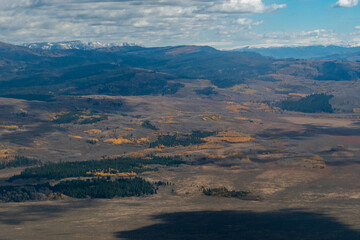 Aerial view of rolling foothills in Jackson Hole valley, showcasing autumn foliage. Landscape features a mix of gently undulating terrain with patches of forested areas displaying vibrant fall colors