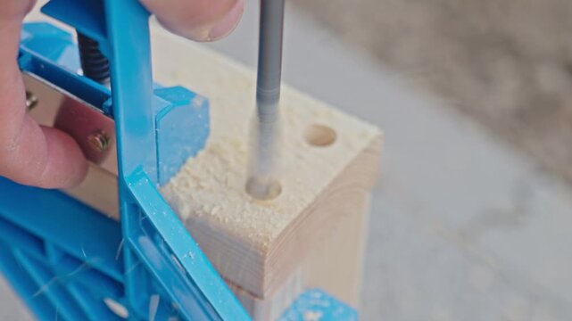 Drill bit creates hole in wooden block using blue pocket hole jig for accuracy. Concept of furniture making or DIY