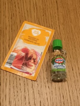 Baking Powder Packet and Almond Flavoring Bottle on Wooden Surface