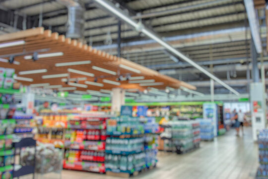 Out of focus image of a modern supermarket interior with colorful shelves full of grocery items. The blurred view includes water bottles, snacks, and general store goods.