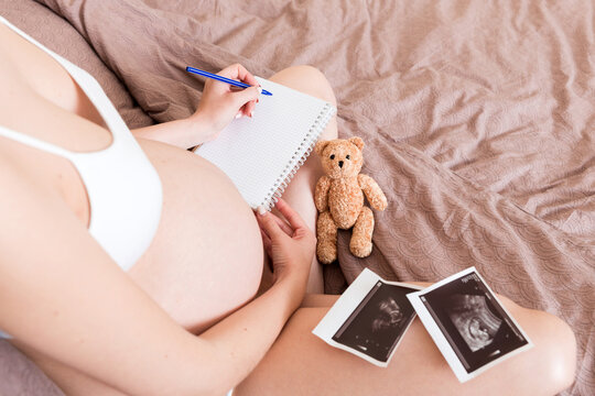Top view caring future mother writing diary with ultrasound. pregnant woman tummy making notes feeling during pregnancy or creating scrapbook - Powered by Adobe