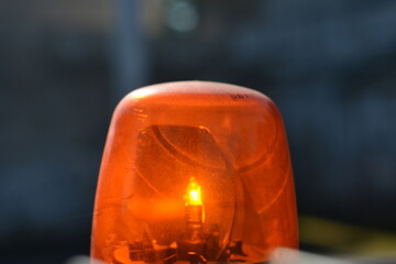 A vibrant close-up shot of an active orange emergency light, illuminating its internal bulb and casting a bright glow against a dark, blurred background, suggesting a moment of alert or warning