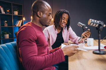 Two African American male podcasters creating audio content in home studio, discussing and reading...