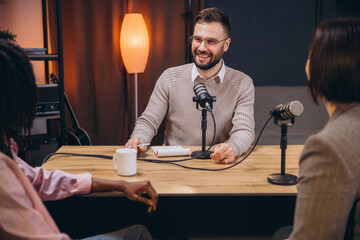 Podcast host interviewing two guests in a professional studio, engaging in a conversation for their audio show