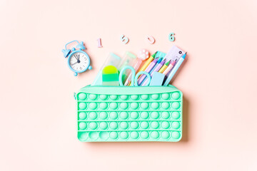 Back to school supplies in a mint green pop-it pencil case with numbers and a blue clock on a pink background.