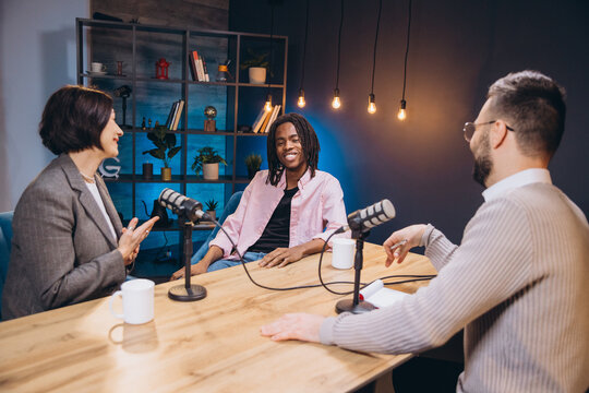 Professional podcast team recording live, discussing topics while sitting around studio table with microphones and broadcasting gear