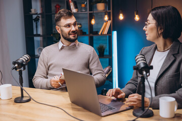 Two podcasters, a man and a woman, are recording a new episode in a professional studio, using a...