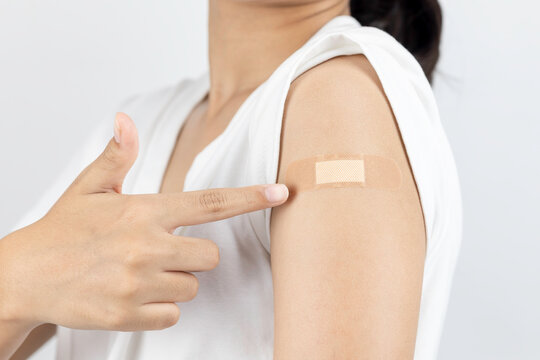 Woman pointing to her arm with a bandage after vaccination. Patient showing plaster after getting Covid-19 or flu vaccine shot for immunity and health. - Powered by Adobe