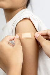 Close up of doctor or nurse applying adhesive bandage to a patient's arm after vaccination. Concept of immunization, COVID−19 vaccine, and healthcare.