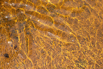Shallow river water with ripples and sun glare on its surface